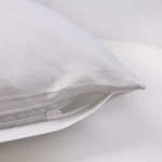 Pościel satyna bawełniana w kolorze białym, widoczna z boku w zbliżeniu. Na zdjęciu znajduje się poszewka na poduszkę z zamkiem błyskawicznym, ukazująca gładką, lekką fakturę materiału. Tło jasne, minimalistyczne.