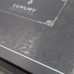 Ekskluzywne opakowanie z ciemnoszarego kartonu z subtelnym wzorem wytłaczanym na powierzchni. Widoczne napisy LUXURY oraz COLLECTION w kolorze srebrnym, umieszczone w centralnej części opakowania, z eleganckim wykończeniem krawędzi.