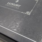 Zbliżenie na eleganckie, czarne opakowanie z wyraźnym, połyskującym wzorem żakardowym w odcieniach srebra. Na górnej części widoczny napis LUXURY COLLECTION. Opakowanie jest zamknięte, z dekoracyjnymi detalami na rogach.