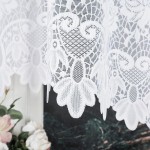 Firana gotowa Demetria żakardowa w kolorze białym o wymiarach 300x160 cm, z delikatnym wzorem florystycznym na dolnej krawędzi. Produkt wiszący, ukazany w zbliżeniu, z tłem w odcieniu ciemnej zieleni i różowych kwiatów.