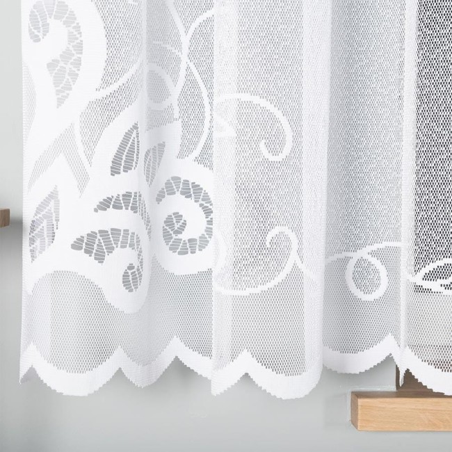 Firana żakardowa, biała, o wymiarach 400x160 cm, z subtelnym wzorem w formie falistych linii. Ujęcie frontalne, wisząca na drewnianym karniszu, tło jednolite, szare. Krawędź firany ozdobnie wykończona falą.