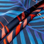 Pościel satyna bawełniana 220x200 w kolorze granatowym, zdobiona dużym, wielobarwnym wzorem w palmowe liście. Ujęcie z boku, ukazujące zamek błyskawiczny. Produkt leży rozłożony, prezentując intensywne odcienie niebieskiego, pomarańczowego i czerwonego.