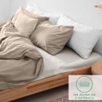 Prześcieradło flanelowe z gumką w kolorze kremowym, rozmiar 180x200 cm, leżące na łóżku z poduszkami. Widać jego gładką fakturę oraz mocowanie. W tle prosta aranżacja sypialni, na podłodze naturalne drewno.