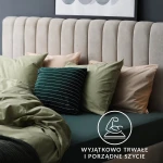 Prześcieradło jersey z gumką 140x200 w kolorze niebieskim, leżące na łóżku z beżowym zagłówkiem. Widoczne poduszki w odcieniach zieleni i beżu, z różnymi wzorami. Efektowna aranżacja sypialni z dekoracyjnym tłem i miękkim materiałem prześcieradła.