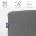 Prześcieradło jersey z gumką 200x220 w kolorze szarym, z widocznym logo, złożone w prostokąt. Tkanina nie wymaga prasowania i nie gniecie się, umieszczone na jasnym tle. Tekstura materiału miękka i gładka.