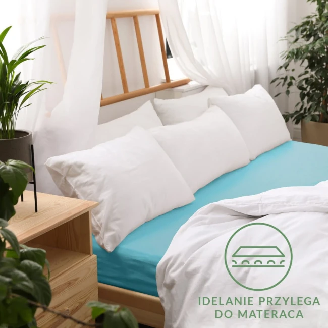 Prześcieradło jersey z gumką w kolorze turkusowym, o wymiarach 180x200 cm, umieszczone na łóżku z jasnym, drewnianym stelażem. W tle białe poduszki oraz zasłony. Widoczna etykieta z napisem Idealnie przylega do materaca. Roślinność w doniczce obok.