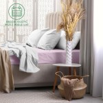 Prześcieradło frotte z gumką 140x200 w kolorze wrzosowym, rozłożone na materacu z szarego tapicerowanego łóżka. W tle widoczna jasna narzuta i poduszki, a obok stoliczek z białą wazonem i suszonymi kwiatami. Tekstura miękka i elastyczna.