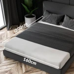 Prześcieradło frotte z gumką o wymiarach 160x200 cm w kolorze popielatym, ułożone na łóżku z widocznymi poduszkami. Tkanina ma gwarantować trwałość oraz elastyczność. Ujęcie z góry, na tle ciemnej ramy łóżka i naturalnych elementów wystroju.