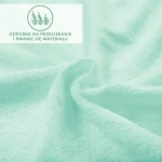 Prześcieradło frotte z gumką w kolorze błękitnym, z widoczną fakturą i delikatnymi włóknami. Ujęcie z bliska na złożony materiał, prezentujący elastyczność i odporność na przecieranie. Na tle widać informację o właściwościach materiału.