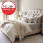 Prześcieradło jersey z elastanem w kolorze niebieskim, rozmiar 200x220, leży na łóżku, obok biała narzuta i poduszki. Tło to jasny, minimalistyczny pokój z beżowym łóżkiem i lampą. Widoczne detale tkaniny i faktura materiału.