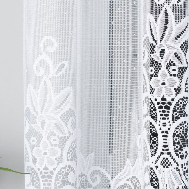 Firana żakardowa Berenika w kolorze białym o wymiarach 300x160 cm, zawieszona w pionie, z delikatnym, koronkowym wzorem. Tło proste, na jasnym, neutralnym tle, podkreślającym detale faktury i wzorów.