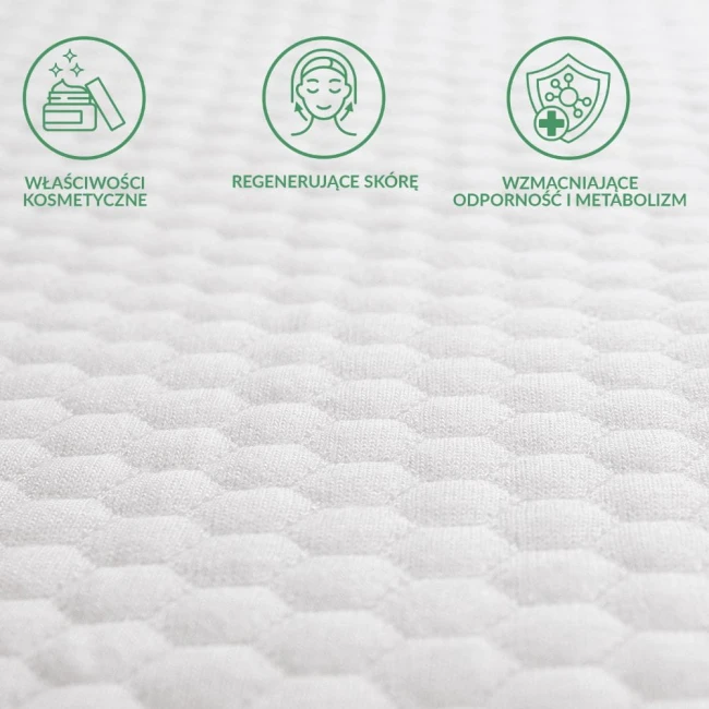 Ochraniacz na materac 90x200 pikowany w kolorze białym, wykonany z teksturowanego materiału. Zbliżenie na fakturę, pokazujące hexagonalne wzory. W tle ikony informujące o właściwościach kosmetycznych, regenerujących skórę i wspierających metabolizm.
