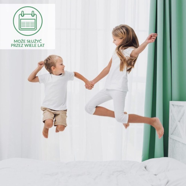Ochraniacz na materac 80x200 Robson w kolorze białym, używany przez dzieci skaczące na łóżku. Widoczny materac z białą narzutą na jasnym tle, obok jasne firany i zielona zasłona, dzieci w białych koszulkach i spodeniach.