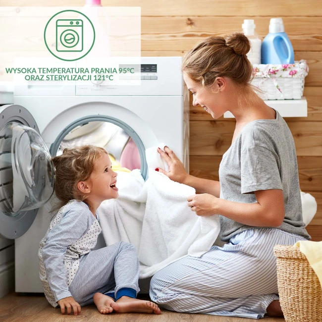 Ochraniacz na materac 90x200, biały, rozłożony na podłożu, z widocznościami na teksturę materiału. Ujęcie frontalne, na wprost, ze szczegółami haftu lub zszywek. W tle pralka oraz kosz na bieliznę, co sugeruje kontekst prania.