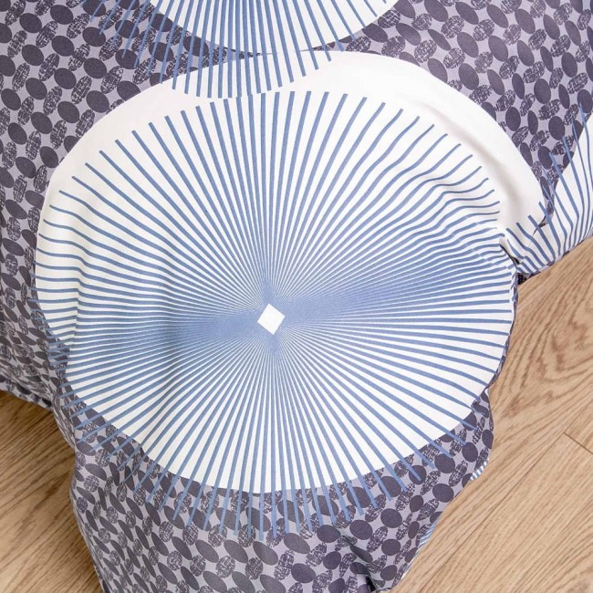 Biała pościel satynowa w rozmiarze 200x220 cm z niebieskimi okręgami i liniami. Kąt ujęcia: z góry, ukazujący wzór i fakturę. Tło jasne, podłoga drewniana. Pościel rozłożona na powierzchni.