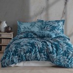 Pościel satyna bawełniana 160x200 Luxury Premium Irene, w odcieniu błękitu, z delikatnym wzorem liści w jasnych tonach. Pościel rozłożona na łóżku, widok z góry, z dwoma poduszkami. Tło w kolorze naturalnego kamienia, akcesoria w drewnie obok.