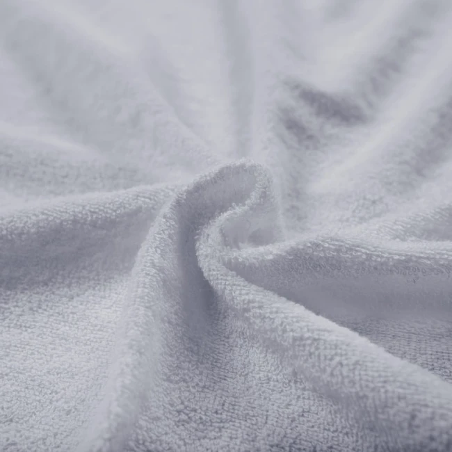 Poszewka frotte 40x40 w kolorze popiel jest rozłożona, ukazując teksturę miękkiego i przyjemnego materiału. Kąt ujęcia to zbliżenie, eksponujące detale splotu tkaniny. Tło jest jasne i uniwersalne, co podkreśla cechy poszewki.