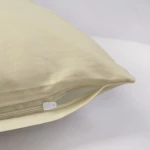 Poszewka satynowa 50x70 w kolorze kremowym, leżąca na białym tle, z widocznym zamkiem błyskawicznym. Materiał gładki, błyszczący, o delikatnej strukturze. Ujęcie z boku, pokazujące kształt i krawędzie poszewki.
