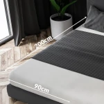 Prześcieradło jersey z gumką w kolorze białym, rozmiar 90x200 cm, leży na łóżku. Widoczna faktura materiału oraz oznaczenia wymiarów, w tle roślina w doniczce i zasłony. Prześcieradło idealnie dopasowane do materaca.