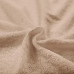 Pościel frotte w kolorze beżowym, rozłożona na miękkiej powierzchni. Widoczna struktura materiału z wyraźną teksturą frotte, w drobnym zbliżeniu, podkreślająca miękkość i komfort. Idealna do aranżacji sypialni.