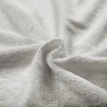 Szara pościel frotte 160x200, prezentująca gładką, teksturowaną powierzchnię. Ułożona w lekki sposób, podkreślająca miękkość materiału. Brak widocznych napisów i logo. Zdjęcie na prostym tle, co uwydatnia detal i fakturę tkaniny.