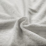 Pościel frotte w kolorze popielatym, w zbliżeniu, ukazująca teksturę materiału o miękkiej, puchatej powierzchni. Widoczny jest efekt falowania materiału, co podkreśla jego elastyczność i grubość. Produkt leży na jednolitym tle.