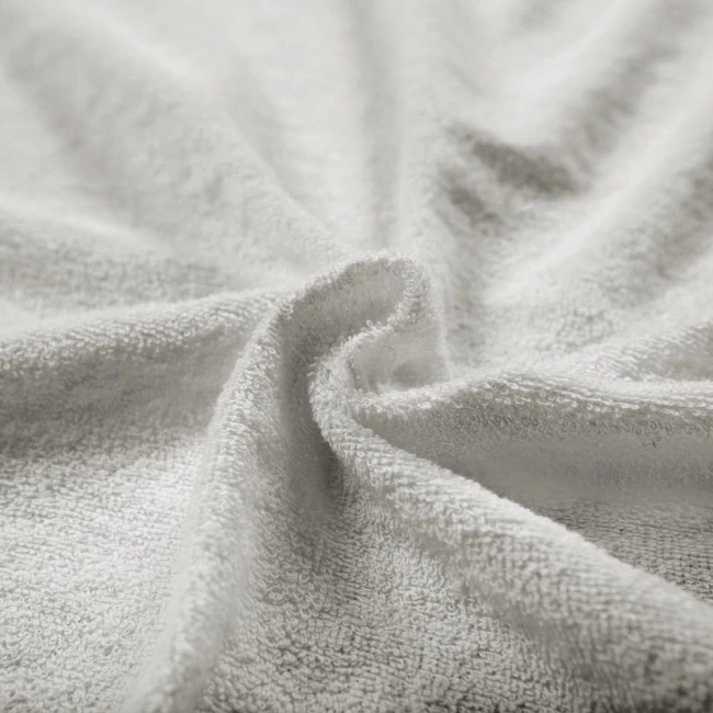 Pościel frotte w kolorze popielatym, w zbliżeniu, ukazująca teksturę materiału o miękkiej, puchatej powierzchni. Widoczny jest efekt falowania materiału, co podkreśla jego elastyczność i grubość. Produkt leży na jednolitym tle.