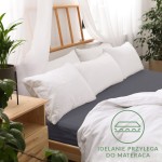 Prześcieradło jersey z gumką 200x220 w kolorze ciemnoszarym ułożone na podłożu łóżka. Widoczne białe poduszki oraz prześcieradło w białym kolorze.