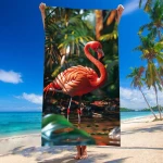 Ręcznik plażowy 100x180 cm z mikrofibry z motywem flaminga w intensywnym różowym kolorze. Ułożony pionowo, trzymany przez osobę na tle plaży z palmami. Wzór flaminga i roślinności nadaje letni klimat. Szybkoschnący materiał, idealny na plażę.