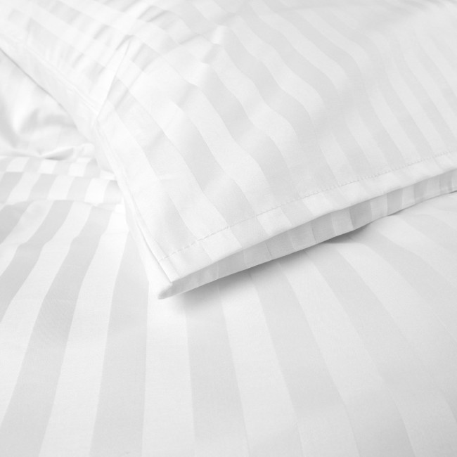 Pościel hotelowa bawełniana 160x200, biała w pasy 2-cm, z zakładką 30 cm. Ułożona na łóżku, w zbliżeniu na detal. Widoczne wyraźne pasy w tle, gładka faktura materiału, poduszka i kołdra z równym wykończeniem.