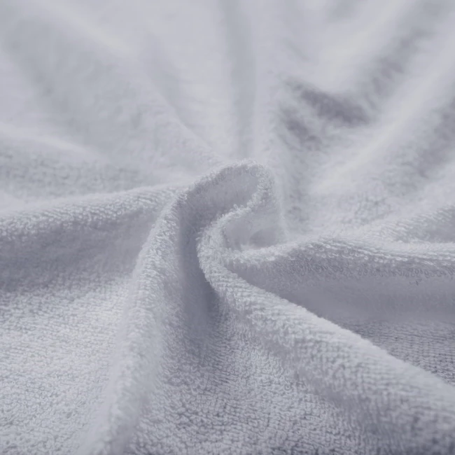 Pościel frotte w kolorze jasno szarym, popiel, składająca się z jednego prześcieradła 200x220 cm oraz dwóch poszewek 80x80 cm. Materiał teksturowany, delikatny w dotyku, ukazany w zbliżeniu, na lekko pofałdowanej powierzchni.