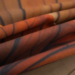 Beżowa pościel satynowa 200x200 Satynlove Premium z liściastym wzorem. Ułożona w fałdy, ukazująca gładką, połyskującą teksturę. Zbliżenie na detale wzoru z ciemnymi akcentami w kształcie gałęzi.