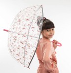 Parasol młodzieżowy, przeźroczysty, z długim uchwytem w różowym kolorze. Zdobiony wzorami jednorożców i tęczy. Ujęcie z boku, parasol trzymany przez dziewczynkę, która stoi uśmiechnięta. Tło proste, białe, co podkreśla kolorowe detale parasola.