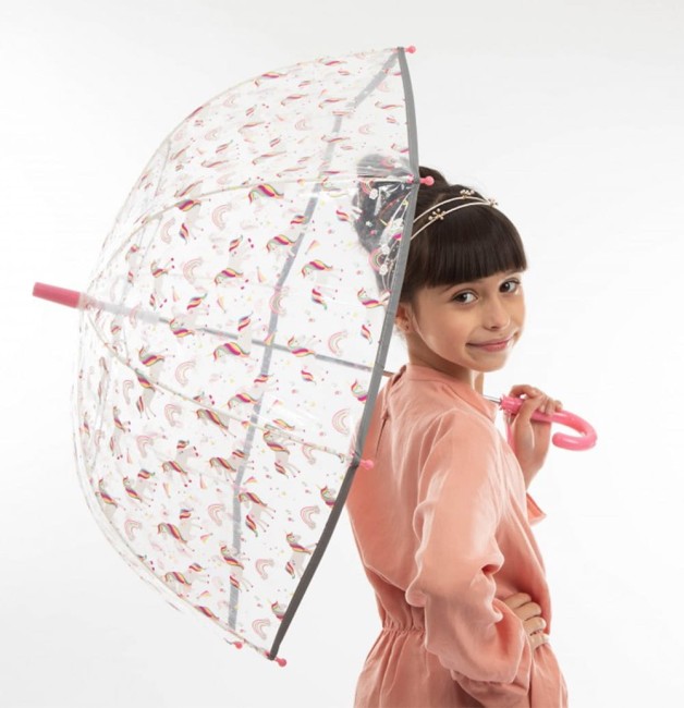 Parasol młodzieżowy, przeźroczysty, z długim uchwytem w różowym kolorze. Zdobiony wzorami jednorożców i tęczy. Ujęcie z boku, parasol trzymany przez dziewczynkę, która stoi uśmiechnięta. Tło proste, białe, co podkreśla kolorowe detale parasola.